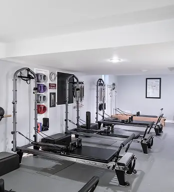 A row of Reformers and Tower units along the wall of the ABS Pilates studio, with springs and props on a rack