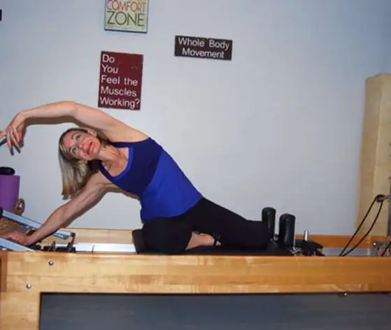 Amanda Smith demonstrating a kneeling side stretch on the Reformer beside the studio's motivational wall signs